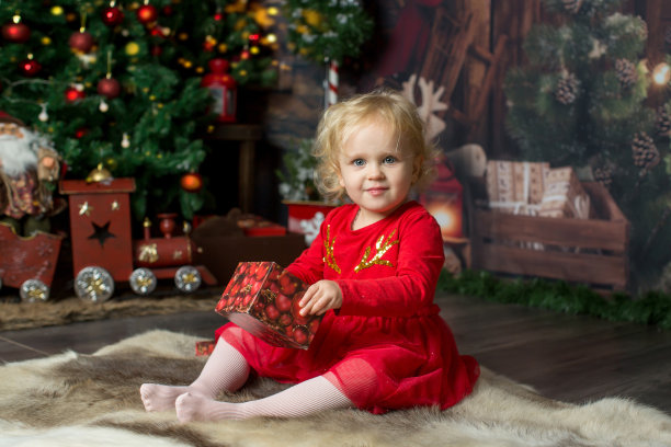 可爱的金发小女孩，卷发女孩，坐在装饰着圣诞装饰的木屋里，打开礼物图片下载