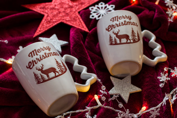 两个圣诞快乐的杯子，红色的毯子上有灯光和装饰图片下载