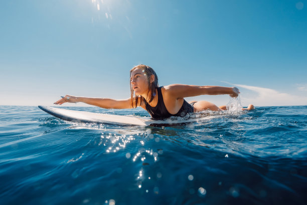 冲浪女孩在冲浪板上划船。迷人的冲浪女人在海洋和阳光的日子图片下载