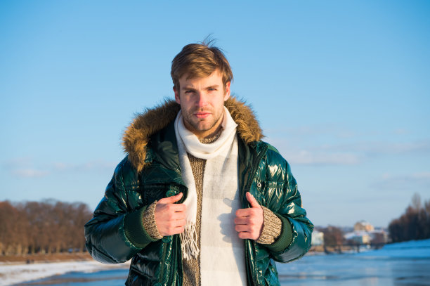 摆姿势的照片。帅哥绿色羽绒服。男人喜欢阳光明媚的冬日。男性季节性时尚。感冒和流感。男式羽绒服，带毛兜帽。感觉温暖舒适。最喜欢的季节图片下载