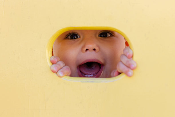 可爱的小男孩在儿童游乐场玩。小孩从黄洞望向摄影机图片下载