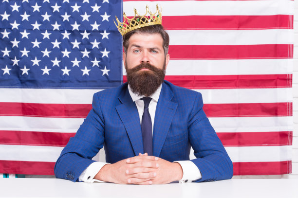 声誉卓著的商人帅哥坐办公桌美国国旗背景，美国梦概念图片下载