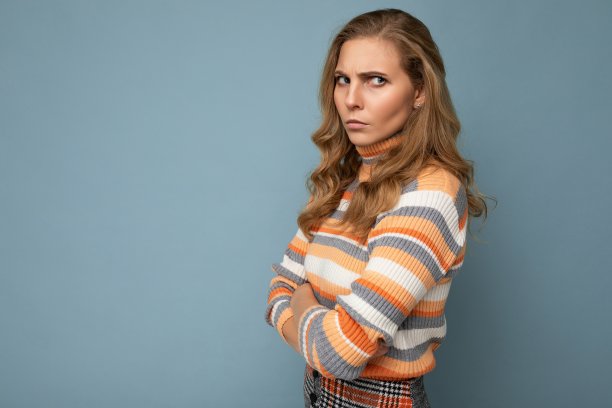 年轻、漂亮、漂亮、有吸引力的肖像照片，愤怒、不快乐、不满意的金发女人，卷发，穿条纹毛衣，蓝色背景，有文字的自由空间图片下载