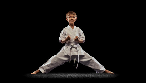 全长肖像的运动小男孩在白色和服摆姿势，训练孤立的黑色背景。空手道，柔道，跆拳道图片下载