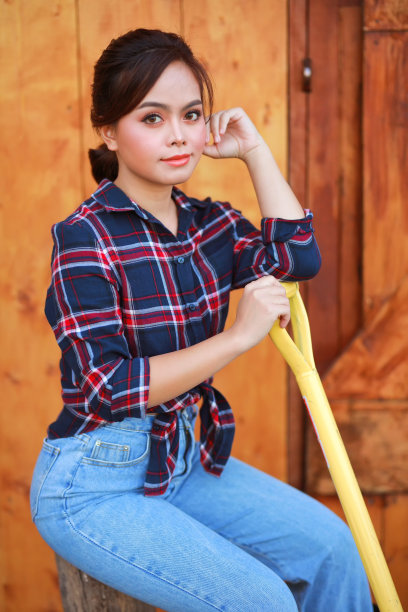 女牛仔的画像。美丽的年轻亚洲女子园丁在红色格子衬衫在夏天日落。图片下载