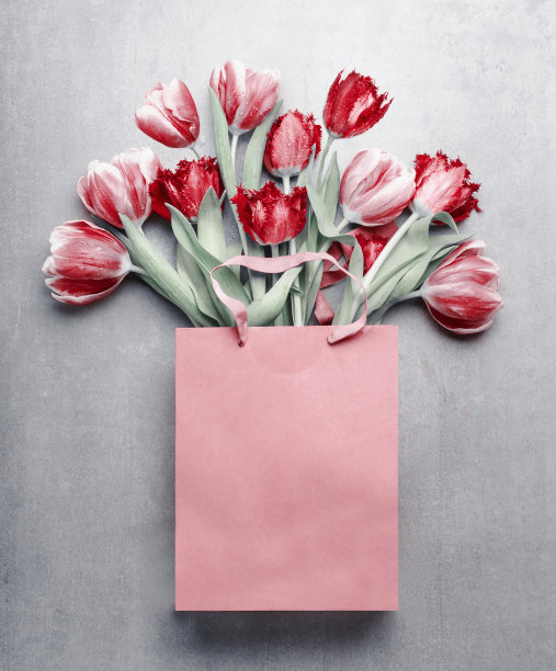 红色郁金香在纸购物袋在灰色的背景。喜庆的春天花束图片下载