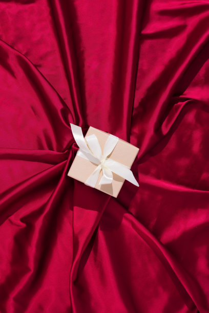 装饰金色礼品盒与蝴蝶结和丝带。妇女节、生日、情人节或圣诞贺卡。俯视图，红色丝绸背景。图片下载