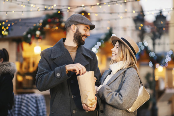 圣诞节的人在街上欢声笑语迎新年。一对幸福的年轻夫妇站在街上，享受着元旦的节日气氛。一个男人拿着一袋爆米花。图片下载