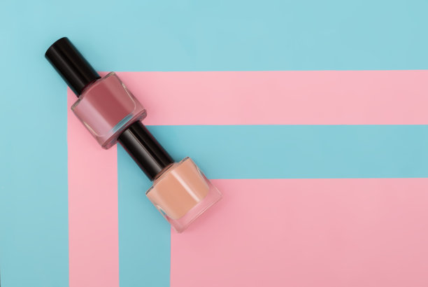粉色和蓝色条纹背景上的两个指甲油瓶。粉色，蓝色和紫色条纹背景指甲油瓶。副本的空间。图片下载