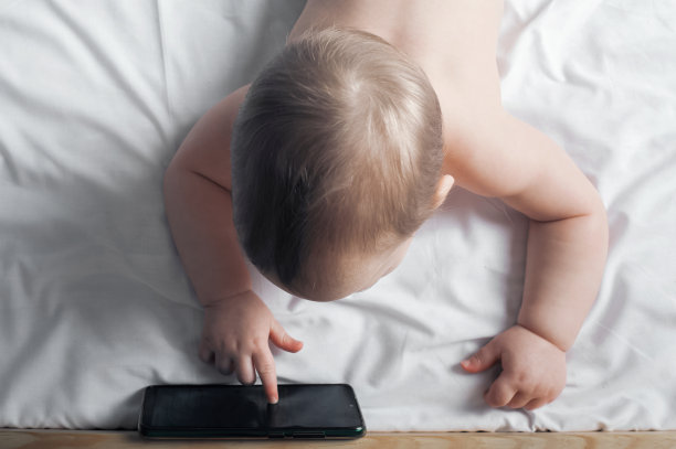 1岁小孩在床上用手机特写。图片下载