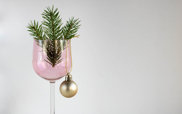 粉色玻璃酒杯，上面有冷杉树枝和白色背景上的金球玩具。圣诞节和新年的概念图片下载