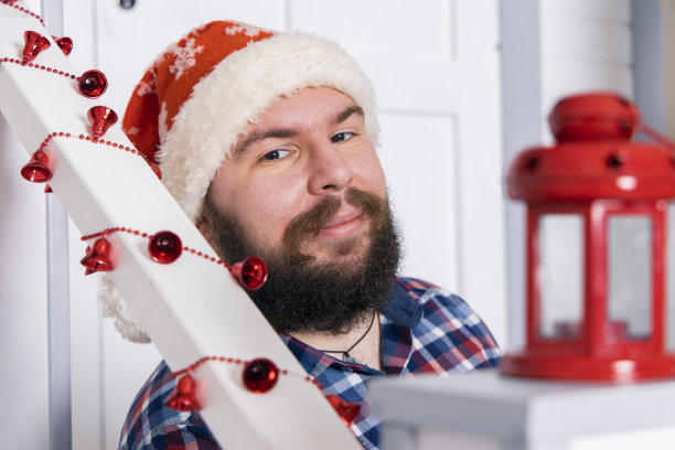 圣诞节期间中年大胡子男人微笑肖像在白色室内用红色装饰节日元素图片下载