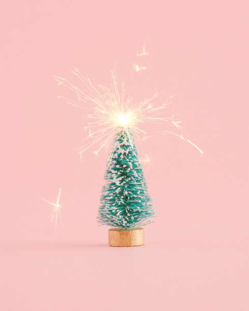 创意布置的圣诞树和 洒水车在柔和的粉红色背景上火花四溅。最小的新年概念。图片下载