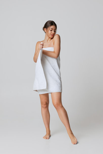 可爱的年轻女孩在白色浴巾独自站在灰色的工作室背景。自然美容，水疗，化妆品图片下载