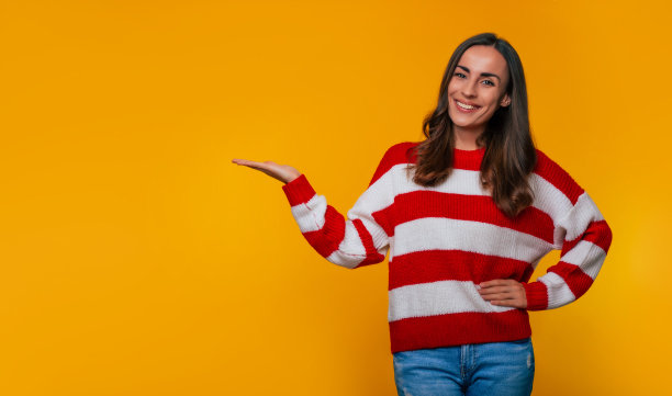 近距离照片，一个美丽的微笑年轻女子在一件毛衣，而她展示了一些东西在手掌广告和孤立的黄色背景图片下载