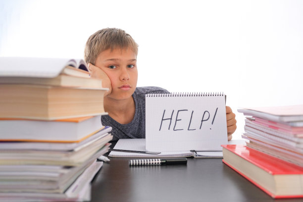 学习困难，学校，隔离教育理念。一个疲惫沮丧的男孩坐在桌子旁，手里拿着许多书。Word帮助打开笔记本。图片下载