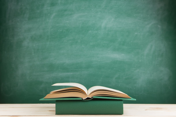 教育与阅读理念——教室里木质桌子上的彩色书籍，背景是黑板图片下载