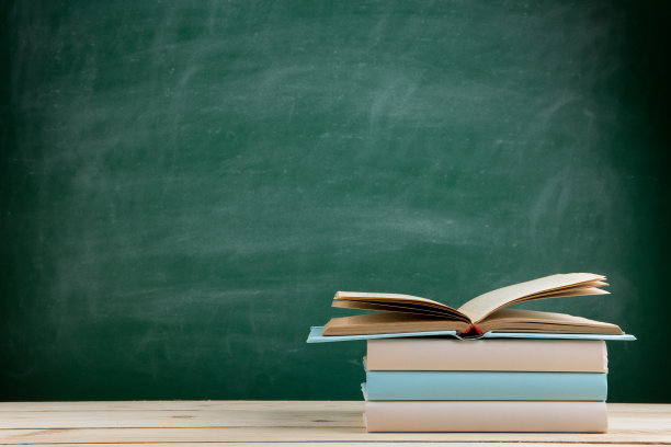 教育与阅读理念——教室里木质桌子上的彩色书籍，背景是黑板图片下载