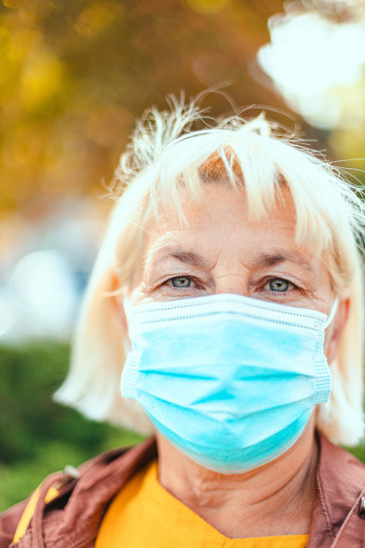 50岁左右的金发成年女人戴着医用口罩看着镜头。垂直取向照片图片下载