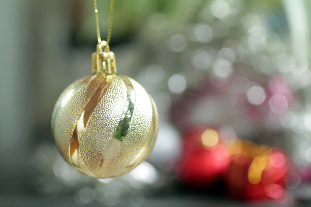 单一的金色圣诞球点缀在模糊的bokeh圣诞灯光背景。图片下载