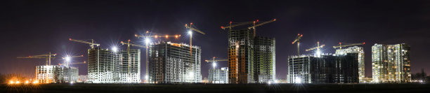 一个大型建筑工地的视图，建筑物正在建设和多层住宅。塔式起重机在夜空背景上活动。全景。图片下载