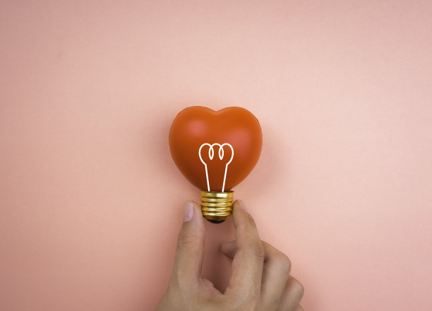 手握灯泡图标符号红心球上粉红色柔和的背景，最小的风格。爱，关心，分享，给予，幸福，灵感和想法概念。图片下载