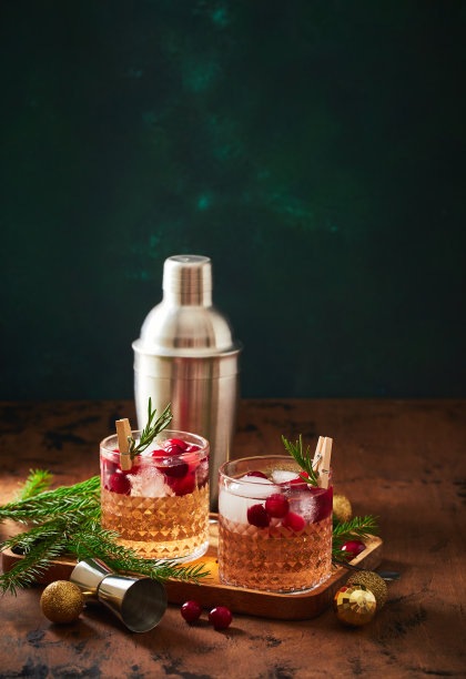 酒精鸡尾酒或非酒精鸡尾酒与伏特加和蔓越莓冰，摇酒器，小调羹，冷杉枝和发光的花环为圣诞的木制背景图片下载