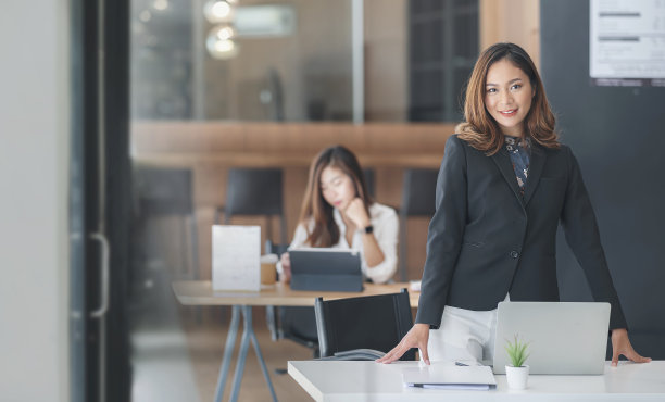 迷人的商人肖像站在她的办公桌前微笑着看着相机。图片下载