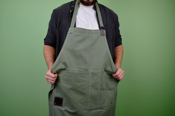 一个穿着厨房围裙的男人。厨师在烹饪中工作。厨师穿着制服、防护服。食品服务方面的工作。专业烹饪。绿色布围裙，休闲时尚的服装。英俊的贝克摆姿势图片下载
