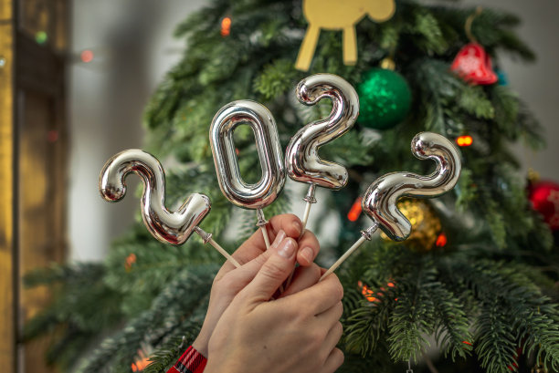 人们手中拿着圣诞树背景上的木棒上的银色数字“2022”。概念新年，贺词贺卡，喜庆气氛图片下载