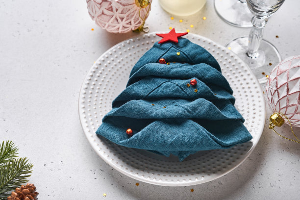 圣诞餐桌设置白色与黑色银器，折叠成圣诞树的餐巾，圣诞银球，香槟，白色背景的圣诞问候眼镜。为文本腾出空间。图片下载