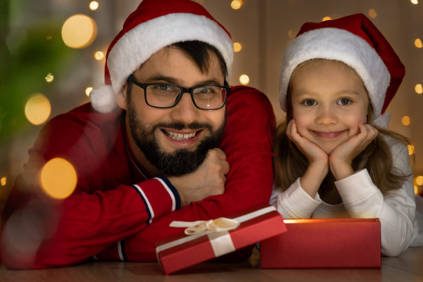 爸爸和女孩看着圣诞树旁的相机，打开盒子。新年图片下载
