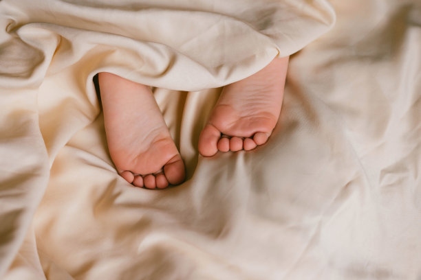 孩子的脚踩在白色的床上。婴儿在他的婴儿床里睡觉。睡眠对婴儿的重要性。睡眠模式婴儿3岁。图片下载