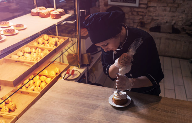 一个糕点师女孩用装着蛋白质奶油的糕点袋装饰酥饼蛋糕，把奶油挤出来。特写镜头图片下载