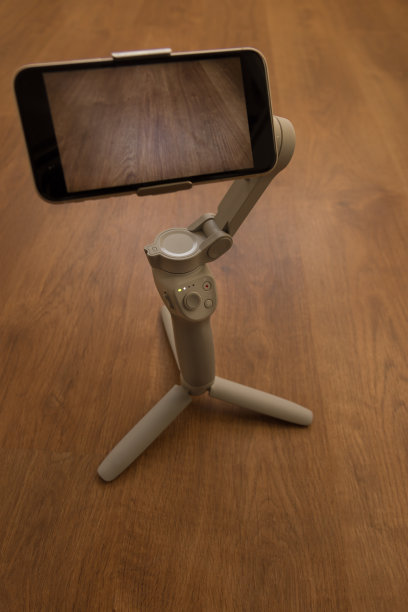 3轴白色稳定器用按钮和led打开，携带手机，在木地板上用三脚架支撑图片下载