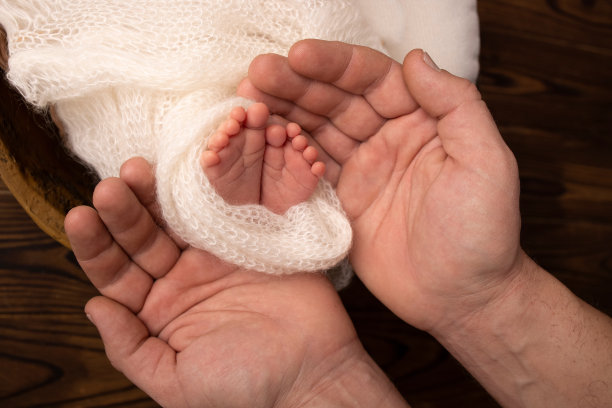 父亲的手掌上，母亲正抱着新生婴儿脚上的白色毯子。新生儿的脚放在父母的手掌上。工作室摄影的一个孩子的脚趾，脚跟和脚。图片下载
