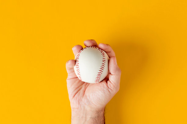 男性手拿着一个黄色背景的棒球。图片下载