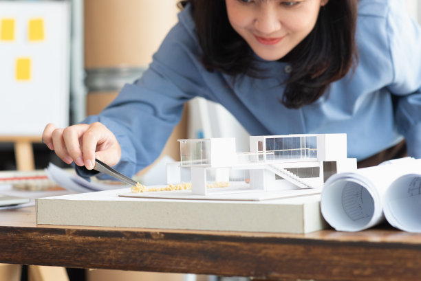 在建筑工作室中，建筑师女性用镊子在现代家庭模型上制作一个模拟灌木，建筑设计师或建筑师学生概念图片下载