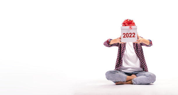 白色背景的年轻女子用写着“2022”的白色礼品盒遮住了自己的脸。这个女孩穿着牛仔裤、衬衫和白色t恤。2022年新年的概念。图片下载