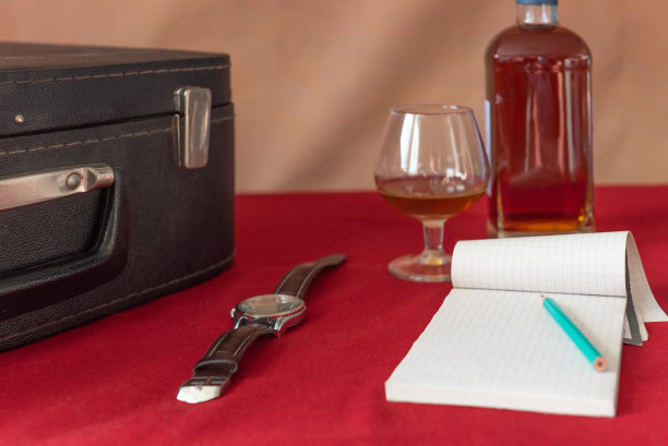 瓶子，玻璃，手表，笔记本，铅笔，手提箱。红色桌布，棕色背景。复古的图片下载