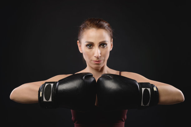 身穿运动服、戴着拳击手套的白人女拳击手，摆出战斗姿势，注视着镜头。在黑暗的背景下。女强人的女斗图片下载