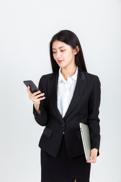 年轻的亚洲妇女穿着黑色的西装，看着智能手机和手提电脑。图片下载