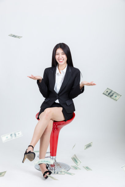 漂亮年轻的亚洲女人坐在椅子上，高兴地与金钱正在下降图片下载