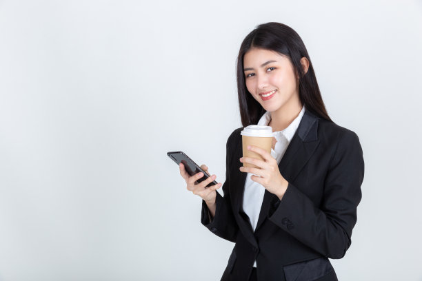 漂亮的年轻亚洲女人拿着咖啡杯和使用智能手机。图片下载