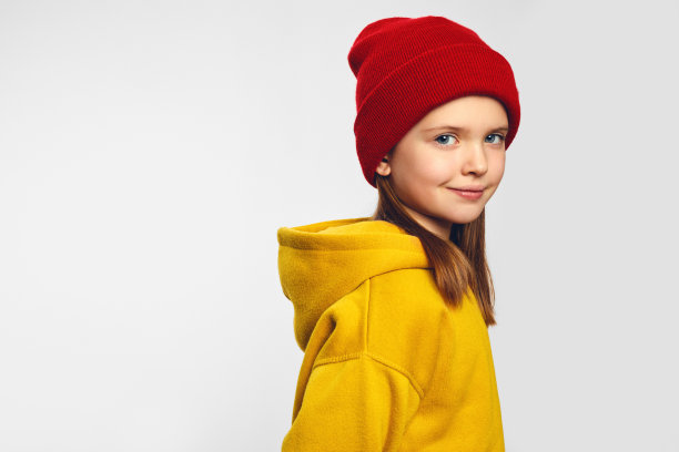 穿着黄色连帽衫，戴着红色帽子的女孩，带着愉快的微笑，站在白色的背景下图片下载