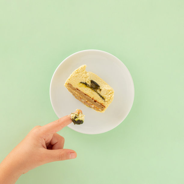 孩子的手指蘸着开心果奶油蛋糕。淡绿色背景下的美味食物的最小场景。健康糖果的概念。平的。邀请卡。生日聚会的想法。图片下载