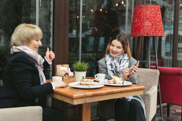 家庭日。一位年迈的母亲和她的成年女儿在街上的一家咖啡馆里使用智能手机。女儿把手机里的照片拿给妈妈看，笑了。图片下载