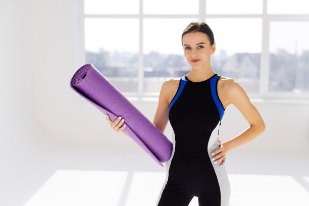 全身照片健康年轻女子在运动服装持有瑜伽垫，而在工作室练习图片下载