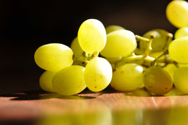 从窗户射进来的阳光照射下，棕色的木头表面上成熟的湿绿葡萄。室内静物画图片下载