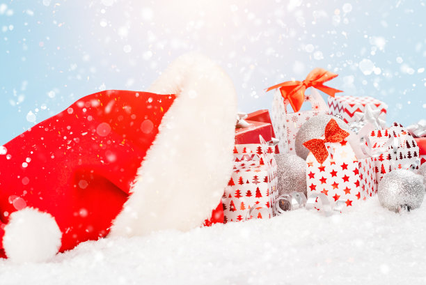 圣诞老人的帽子躺在雪地里，在浅蓝色背景上的各种各样的盒子里装满了新年的节日礼物。新年的概念。圣诞贺卡。图片下载